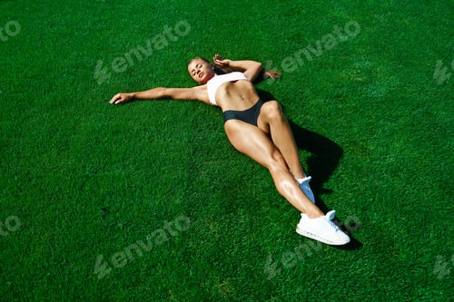 Preview: Fit young woman lying on grass at stadium field