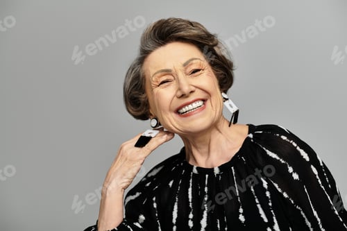 Preview: A beautiful woman in her 60s exudes confidence and charm, dressed elegantly against a grey backdrop.