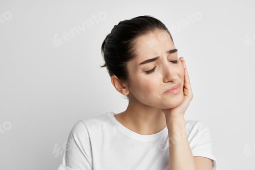 Preview: pretty brunette in white t-shirt holding face headache emotion health problems
