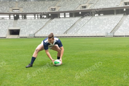 Preview: Rugby ball resting on freshly mown turf inside overcast stadium, near empty grey seats