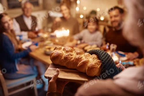 Preview: Close up of mature woman serving Challah bread to her family during dinner on Hanukkah.