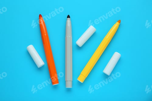 Preview: Different colorful markers and caps on light blue background, flat lay