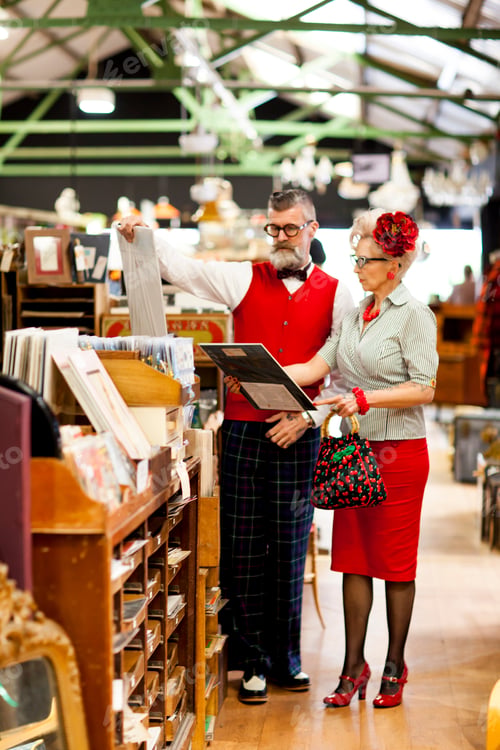 Preview: Quirky vintage couple looking at pictures in antique and vintage emporium
