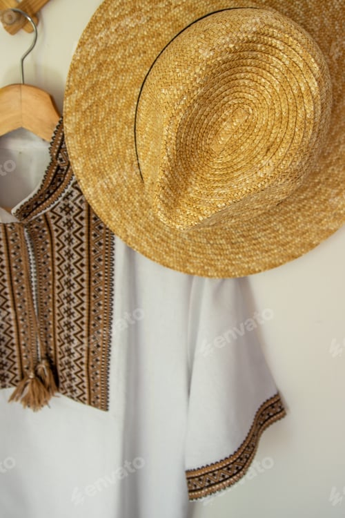 Preview: Ukrainian clothes embroidered shirt. Brown beige and white black threads background. Straw hat