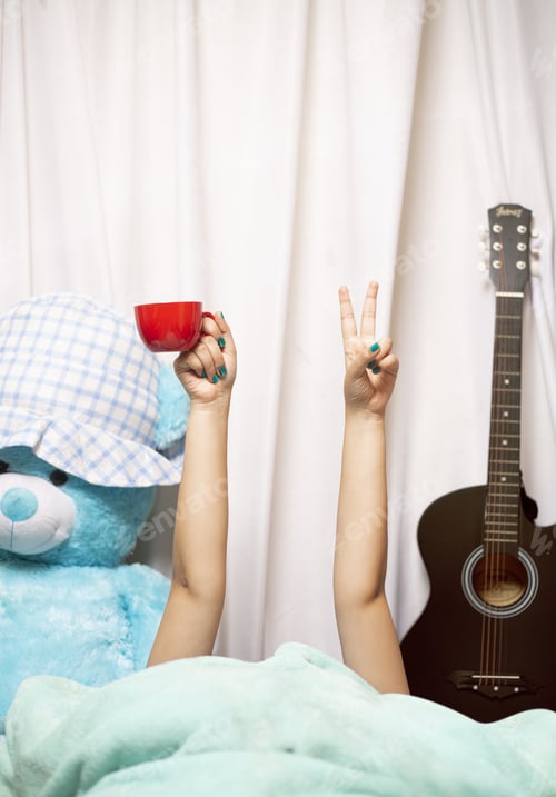 Preview: Vertical shot of woman in bed with coffee cup and piece sign