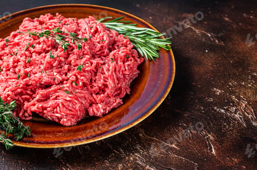 Preview: Raw mince beef and lamb meat on a rustic plate with herbs. Dark background. Top view. Copy space