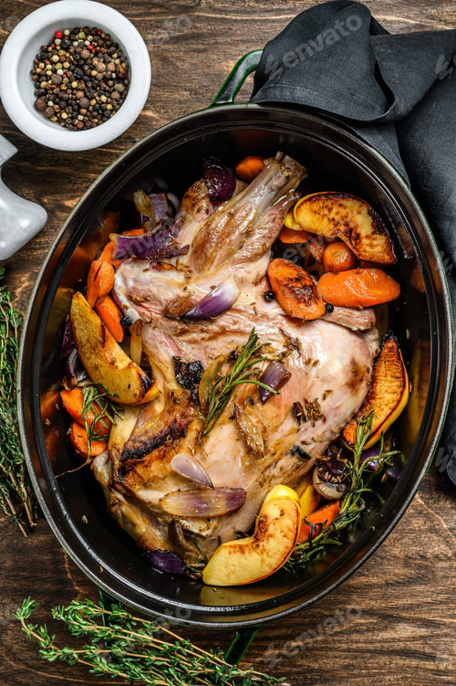 Preview: Baked whole goat shoulder leg in a baking dish. Wooden background. Top view