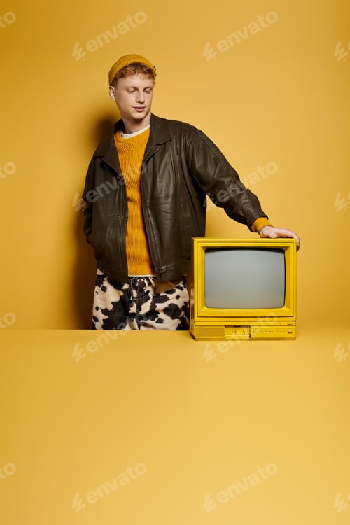 Preview: Trendy young man in a winter outfit poses confidently with a vintage TV in a studio.