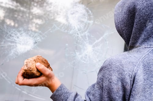 Preview: Child holds a stone to throw it against a glass and break a window.