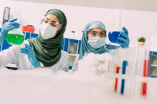 Preview: female muslim scientists in medical masks holding flasks while experimenting with dry ice in