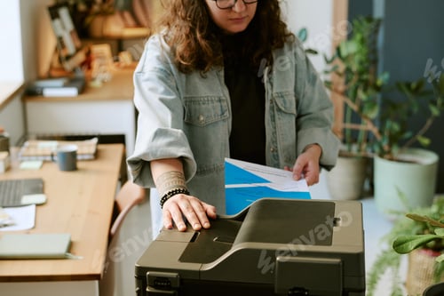 Preview: Young Adult Caucasian Woman Using Printer While Holding Documents in Office
