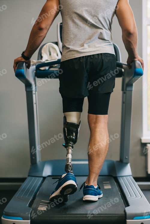 Preview: cropped shot of sportsman with artificial leg walking on treadmill at gym