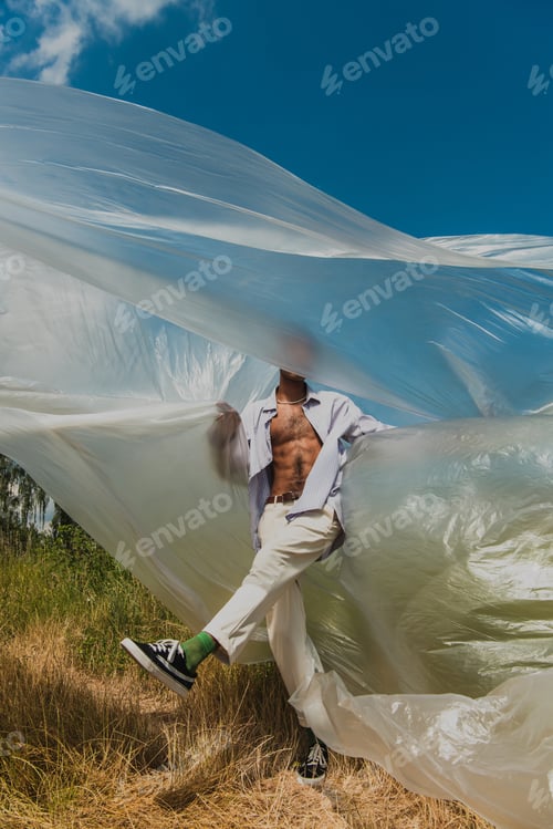 Preview: african american man in white trousers posing under polyethylene in field