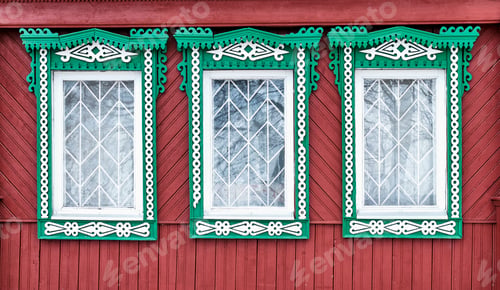 Preview: Three old windows with grilles and carved wooden green-white architraves on red wall from board.