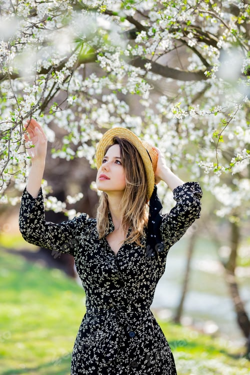 Preview: Young girl in a hat stay near a flowering tree