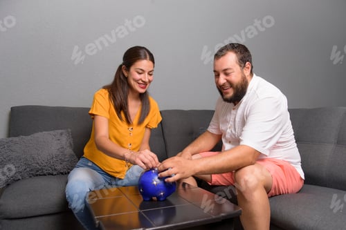Preview: Happy Latin couple saves money in their piggy bank. Savings for investment concept