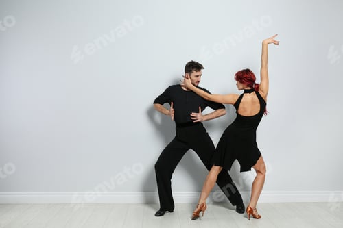 Preview: Beautiful young couple dancing near light wall. Space for text