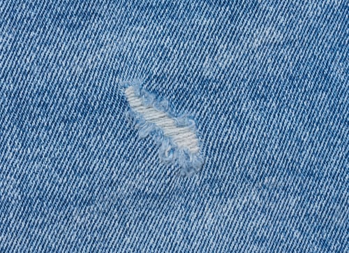 Preview: Fragment of blue jeans fabric with a hole, full frame, close up