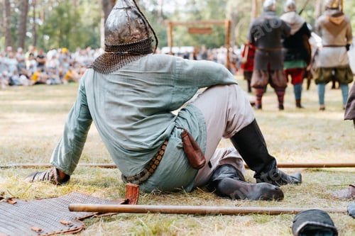 Preview: Viking in a helmet and medieval clothes resting after the battle, sitting on the grass in the forest