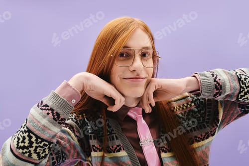 Preview: Stylish young queer man with long red hair poses playfully against a vibrant purple backdrop
