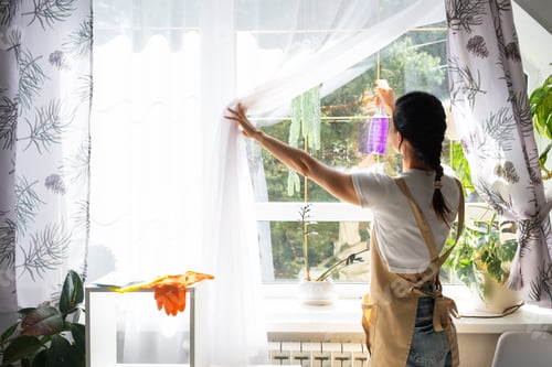Preview: Woman in rubber gloves and apron manually washes window of house with rag cleaner