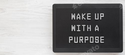 Preview: 'Wake up with a purpose' words on a black lightbox on a white wooden background, top view.