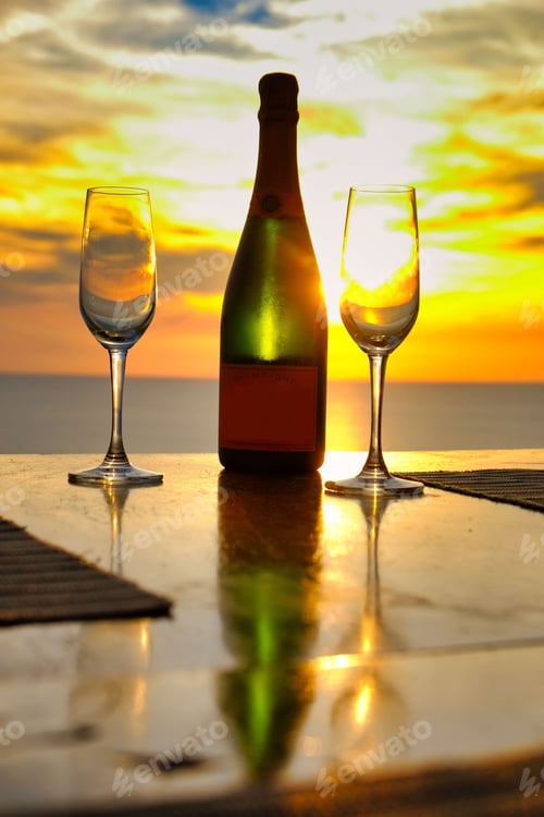 Preview: Vertical shot of two wine glasses and a bottle on the background of a bright yellow sunset