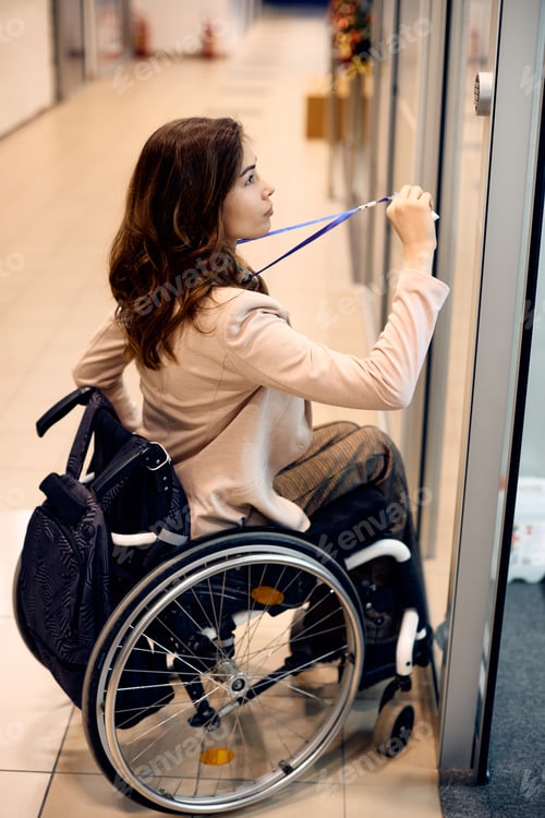 Preview: Young businesswoman in wheelchair unlocking her office door with ID card.