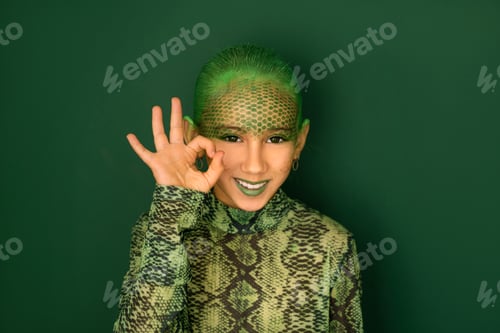 Preview: A beautiful girl in the guise of a green snake gestures with fingers, smiling sweetly at the camera