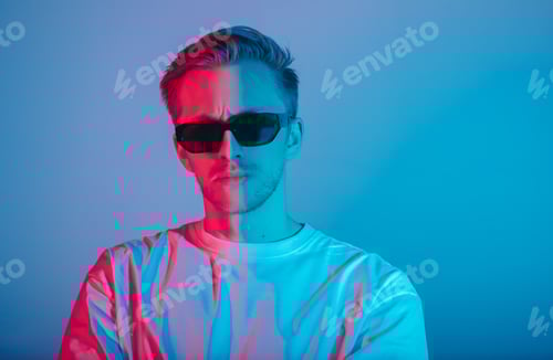 Preview: Portrait of fashion young man in white t-shirt and black sunglasses in red and blue neon light.