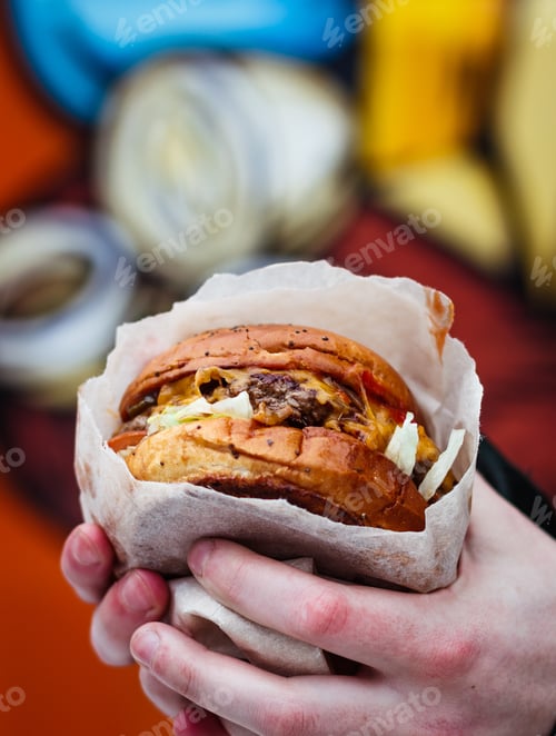 Preview: Vertical selective closeup shot of a person holding a wrapped burger