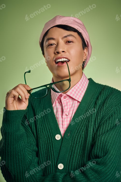Preview: Stylish Asian man in pink checkered shirt and green cardigan poses in vibrant studio