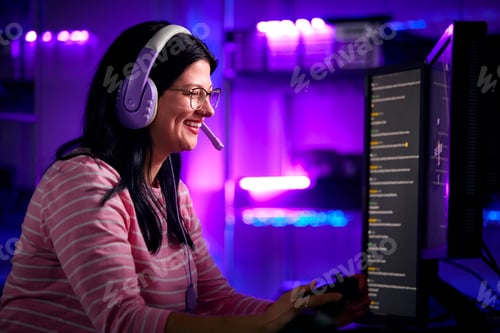 Preview: Low Key Lighting Shot Of Female Gamer In Front Of Computer Screens With Headphones And Controller