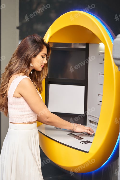 Preview: Stylish woman using an ATM machine outdoors on the street.