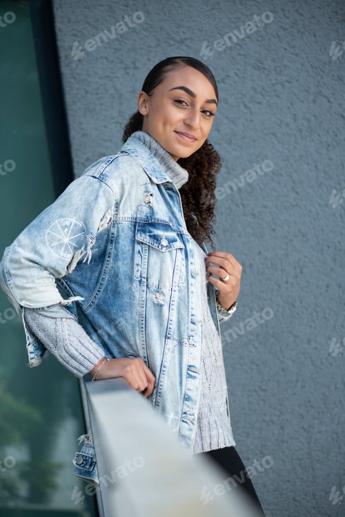 Preview: Confident young woman leaning on a railing with a modern building backdrop.