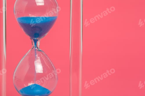 Preview: Hourglass with blue sand on a pink background in a close-up view