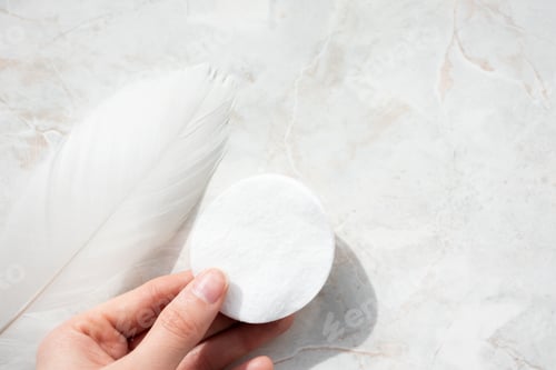 Preview: Woman hand holding cotton pads and feather on marble background