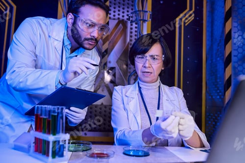 Preview: indian scientist pointing with pan at samples near colleague in futuristic scientific laboratory
