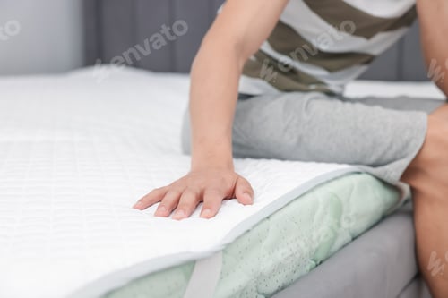 Preview: Man sitting on soft mattress at home, closeup. Space for text
