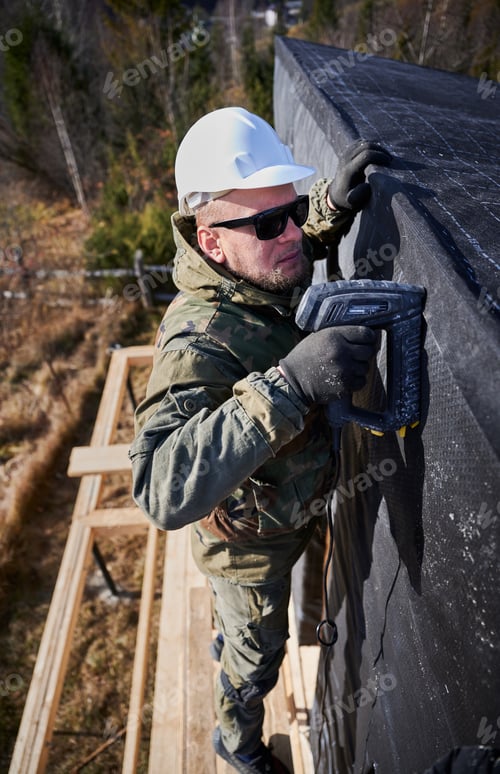 Preview: Male builder installing waterproof membrane on wall of future wooden frame house.