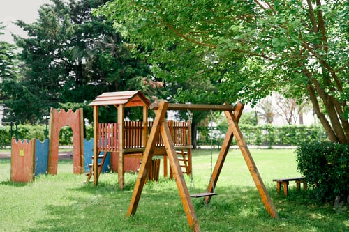 Preview: Wooden playground with swings on a green lawn among the trees