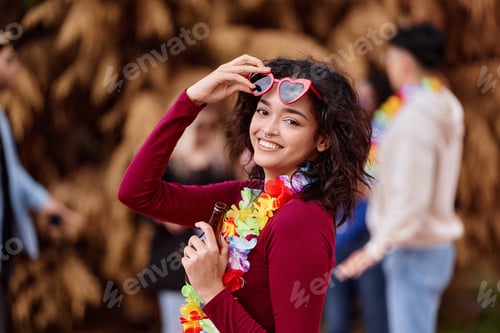 Preview: Happy woman holding a bottle of beer while partying with friends outdoors.