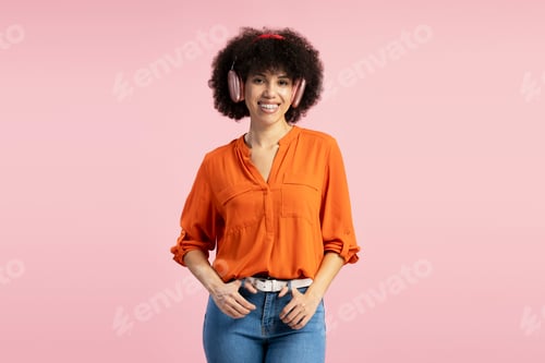 Preview: Young woman wearing headphones listening to music and smiling on pink background