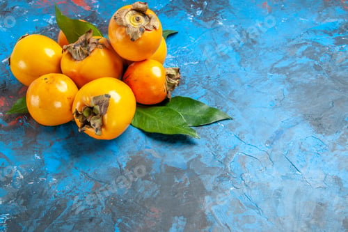 Preview: Front close view of fresh diospyros kaki with leafs on blue table