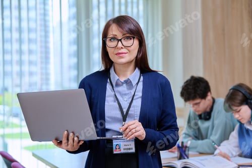 Preview: Portrait of confident middle aged female teacher holding laptop looking at camera