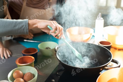 Preview: Hand of young woman with heat resistant spatula mixing ingredients in frying pan