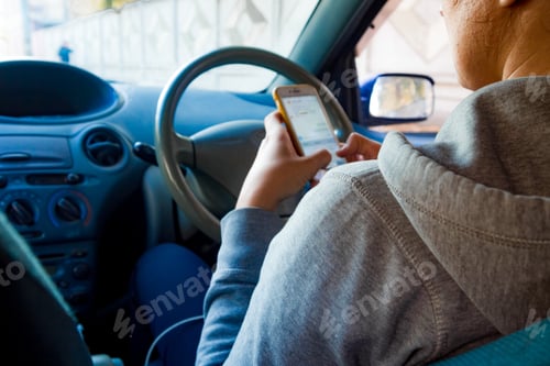 Preview: a young woman sits behind the wheel and looks at the phone in her hand