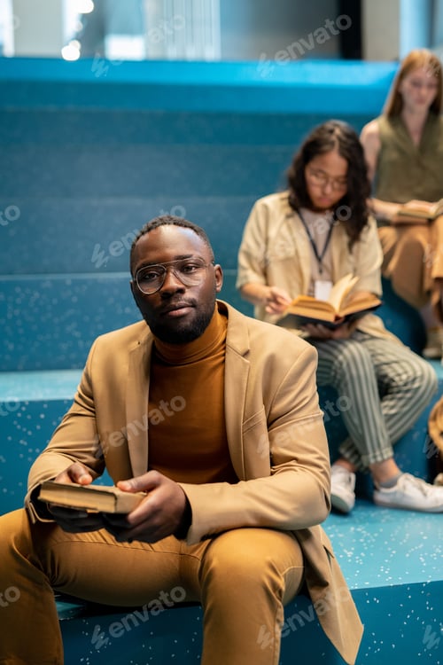 Preview: Young African businessman with book looking at you