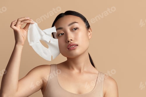 Preview: Woman Face Mask. Portrait Of Asian Girl Removing Cosmetic White Textile Mask