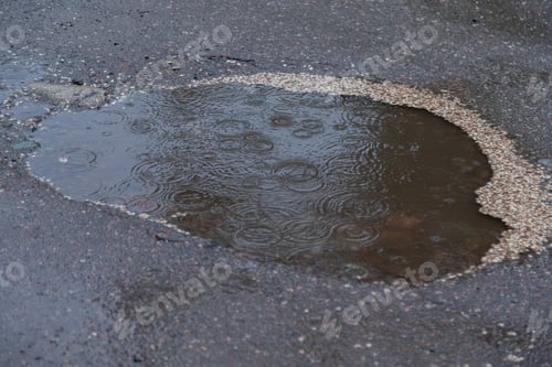 Preview: Closeup of dripping raindrops in a puddle in rainy day